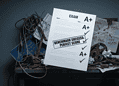 Messy workshop desk with tangled wires and gears, overlaid by an exam sheet showing A+ scores and a 'Benchmark Success: Perfect Score' stamp.