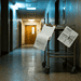 Dim hospital hallway with blue-tinted lighting and a metal cart holding papers and clipboards in the foreground