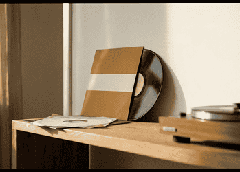 Vinyl records leaning against a wall with a turntable on a wooden shelf, in warm light