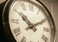 Close-up of an antique clock face with Roman numerals and ornate hands in a sepia tone.