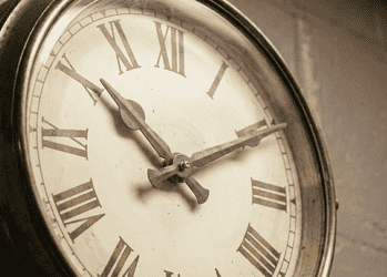Close-up of an antique clock face with Roman numerals and ornate hands in a sepia tone.
