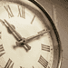 - VeyrZest.com Close-up of an antique clock face with Roman numerals and ornate hands in a sepia tone.