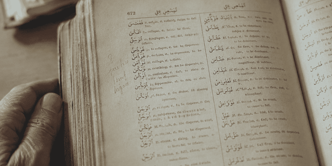Open antique dictionary with Arabic entries, held by a left hand.
