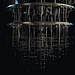 - VeyrZest.com Upside-down metallic, multi-ring machine with numerous cables and tubes hanging from circular frames against a dark background.