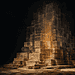 - VeyrZest.com Pyramid-like sculpture made of stacked stone blocks with an inner orange glow, surrounded by a dark background in a gallery setting.
