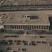 - VeyrZest.com Aerial view of a large rectangular office building with a flat roof, surrounded by parking lots and roads steamrollering around it.