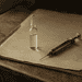 Vintage syringe and a glass vial on a stack of brown paper on a wooden desk.