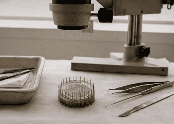 Close-up of a pin ring and precision tools on a lab bench beside a microscope in the background.