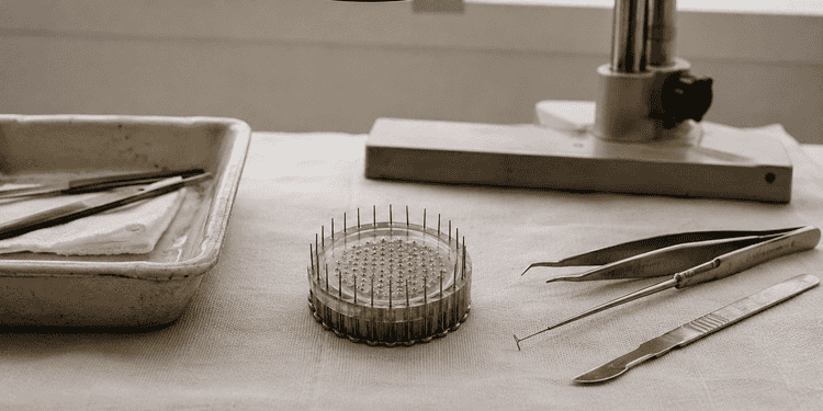 Close-up of a pin ring and precision tools on a lab bench beside a microscope in the background.