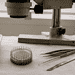 Close-up of a pin ring and precision tools on a lab bench beside a microscope in the background.